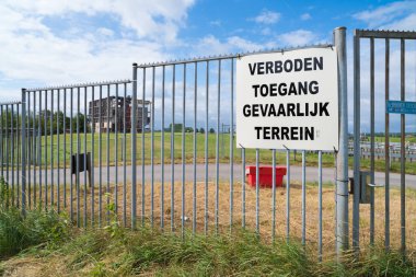 Geçiş yasak, tehlikeli bölge (verboden toegang, gevaarlijk terrein Flaman dilinde) eski bir fabrikanın harabelerinin önünde metal bir çit üzerinde