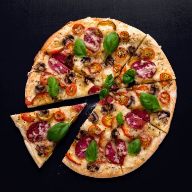 Sıcak ve lezzetli pizza salam domates peynir ve mantarlı siyah bir ahşap arka plan üzerinde yemeye hazır. Üstten Görünüm.