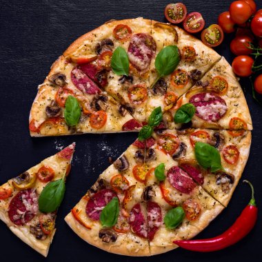 Sıcak ve lezzetli pizza salam domates peynir ve mantarlı siyah bir ahşap arka plan üzerinde yemeye hazır. Üstten Görünüm.