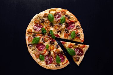 Sıcak ve lezzetli pizza salam domates peynir ve mantarlı siyah bir ahşap arka plan üzerinde yemeye hazır. Üstten Görünüm.