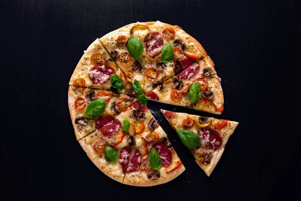 Sıcak ve lezzetli pizza salam domates peynir ve mantarlı siyah bir ahşap arka plan üzerinde yemeye hazır. Üstten Görünüm.