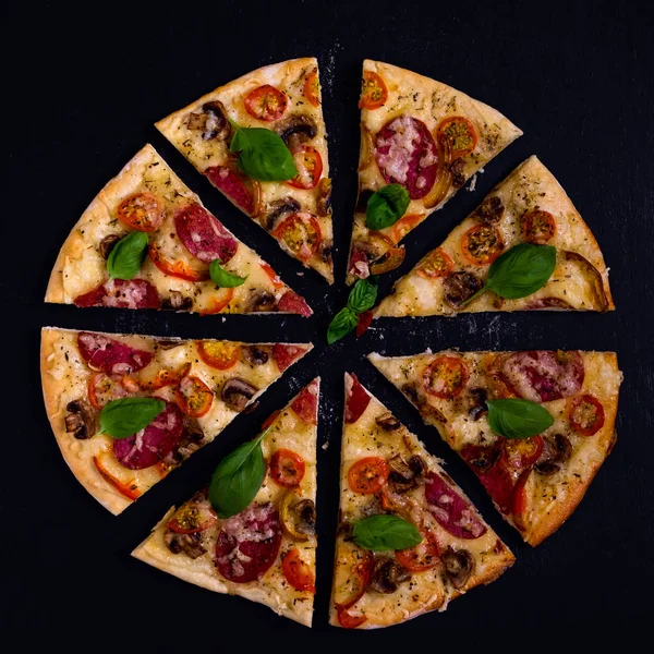 Sıcak ve lezzetli pizza salam domates peynir ve mantarlı siyah bir ahşap arka plan üzerinde yemeye hazır. Üstten Görünüm.