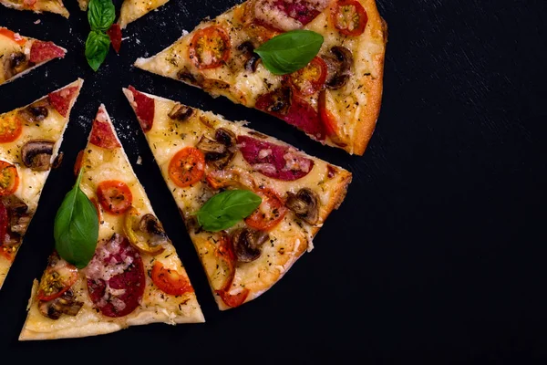 Sıcak ve lezzetli pizza salam domates peynir ve mantarlı siyah bir ahşap arka plan üzerinde yemeye hazır. Üstten Görünüm.
