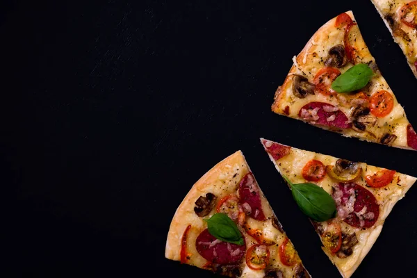 Rodajas de pizza calientes y deliciosas listas para comer sobre un fondo de madera negro . — Foto de Stock