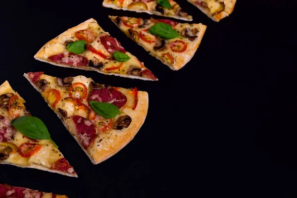 Rodajas de pizza calientes y deliciosas listas para comer sobre un fondo de madera negro . — Foto de Stock