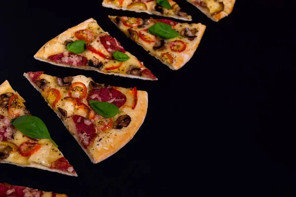 Sıcak ve lezzetli pizza dilimleri bir siyah ahşap arka plan üzerinde yemeye hazır.
