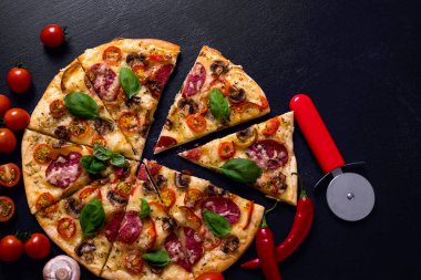 Sıcak ve lezzetli pizza salam domates peynir ve mantarlı siyah bir ahşap arka plan üzerinde yemeye hazır. Üstten Görünüm.