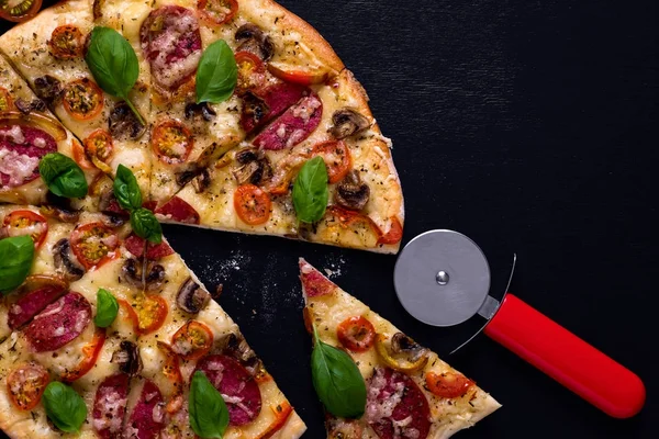 Sıcak ve lezzetli pizza salam domates peynir ve mantarlı siyah bir ahşap arka plan üzerinde yemeye hazır. Üstten Görünüm.
