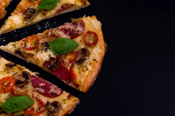 Pizza caliente y deliciosa con queso de tomate salami y champiñones listos para comer sobre un fondo de madera negra. Vista superior . — Foto de Stock