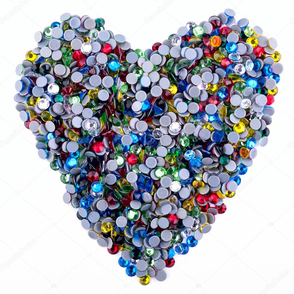 Many colored rhinestones made in the shape of a heart on a white background. Top view.