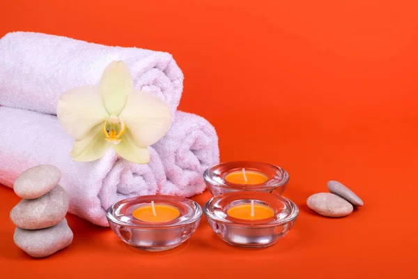 Toalhas, velas e flores de orquídeas para um relaxamento de spa em fundo laranja — Fotografia de Stock