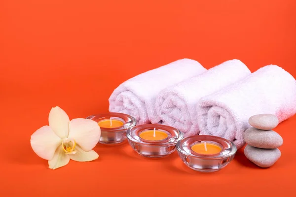 Toalhas, velas e flores de orquídeas para um relaxamento de spa em fundo laranja — Fotografia de Stock