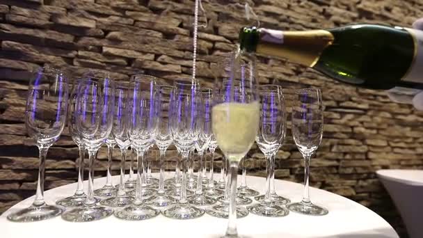 The waiter pours champagne into glasses, champagne glasses on the buffet table, the hall of the restaurant or hotel, the waiters hand in a white glove with a bottle of champagne, indoor, close-up — Stock Video