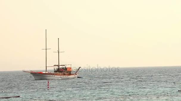 Ιστιοπλοΐα πλοίο πλωτήρες στην θάλασσα, ιστιοπλοϊκό σκάφος, στη θάλασσα με τα πόδια σε ένα ιστιοπλοϊκό σκάφος, σιλουέτα της μοναχική θαλαμηγός χωρίς πανιά και με τους ανθρώπους στον ορίζοντα στο ηλιόλουστο καιρό — Αρχείο Βίντεο