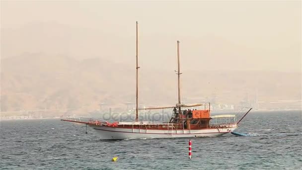 Nave a vela galleggia in mare, yacht a vela, passeggiata in mare su uno yacht a vela, silhouette di yacht solitario senza vele e con persone all'orizzonte con tempo soleggiato — Video Stock