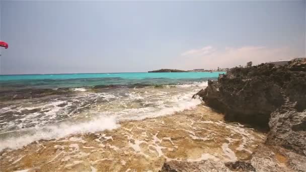 Лазурне море, море берга кольорове, хвилі ламаються на скелястому березі, на тлі берегової лінії — стокове відео