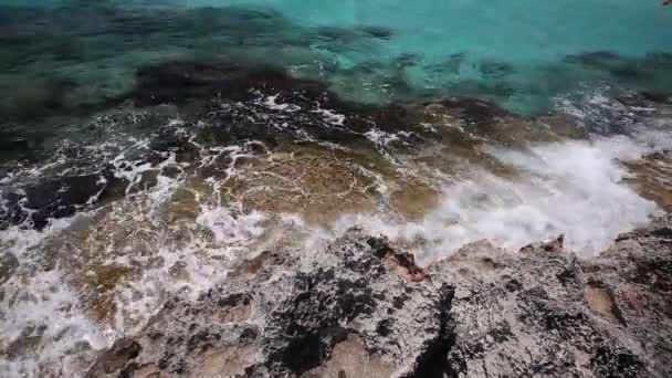 De golven breken tegen de rotsachtige kust, tegen de achtergrond van de kustlijn, de azuurblauwe zee, een zee van berg gekleurde — Stockvideo