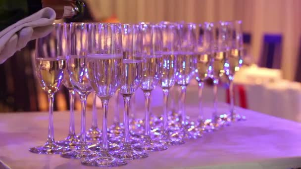 Le serveur verse du champagne dans des verres, des verres de champagne sur la table du buffet, le hall du restaurant ou de l'hôtel, les serveurs donnent un gant blanc avec une bouteille de champagne, intérieur, gros plan — Video