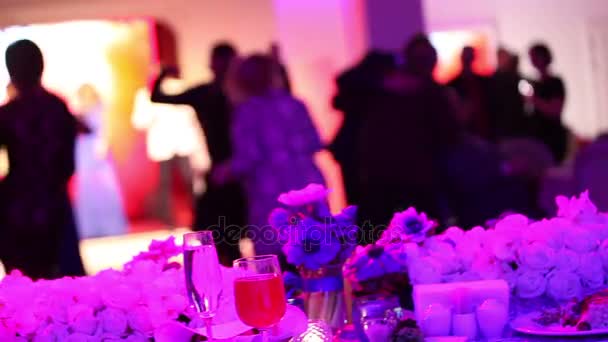 Grupo de personas siluetas bailando en una sala de banquetes oscuros para una recepción de la boda. El banquete de bodas, la gente baila - disparado a través de las decoraciones de mesa de la boda, decoración de la boda — Vídeo de stock
