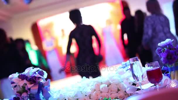 Groupe de personnes en silhouette dansant dans une salle de banquet sombre pour une réception de mariage.Le banquet de mariage, les gens dansent - tiré à travers les décorations de table de mariage, décoration de mariage — Video