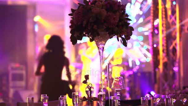 Группа силуэтов танцует в темном банкетном зале для свадебного приема.Свадебный банкет, люди танцуют - снято через украшения свадебного стола, свадебное оформление — стоковое видео