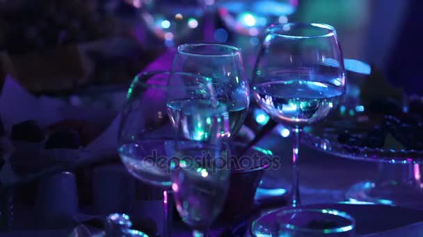 Стеклянные бокалы на столе в ресторане, сценическое освещение, на заднем плане, темная, мелкая глубина резкости, крупный план — стоковое видео