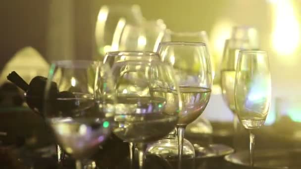 Bicchieri di vetro su un tavolo in un ristorante, illuminazione di scena, sullo sfondo, scuro, profondità di campo poco profonda, primo piano — Video Stock
