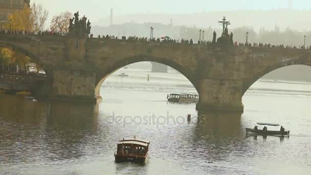 Turistas en el puente Charles, puente Charles. Praga con el telón de fondo de un barco turístico al atardecer — Vídeos de Stock