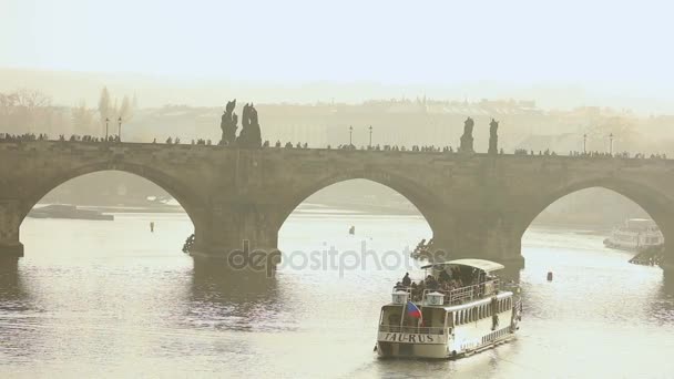 Touristen auf der Karlsbrücke, der Karlsbrücke. Prag vor der Kulisse eines Touristenschiffes bei Sonnenuntergang — Stockvideo