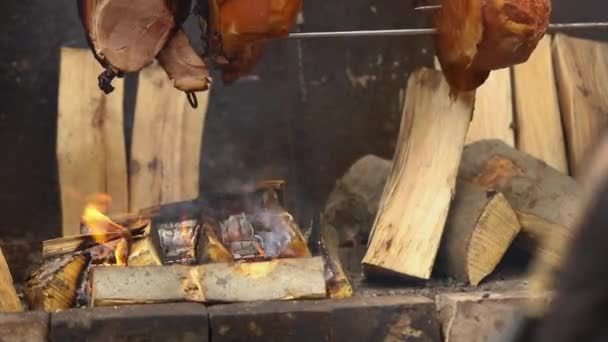 Grandes pedaços de deliciosos presuntos de porco cozidos em uma fogueira. A comida de rua. Comida ao ar livre. Acampar e cozinhar em um cuspo sobre o fogo, o homem cozinha grandes pedaços de carne em um cuspo no fogo, close-up — Vídeo de Stock