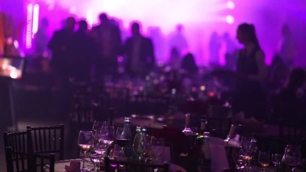 Une fête de jeunesse dans un restaurant ou une boîte de nuit, des tables de banquet avec de l'alcool et de la nourriture sur fond de silhouettes de danseurs, de lumière de scène et de pourpre — Video