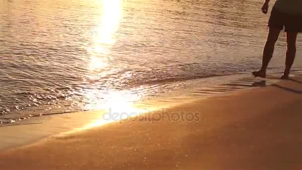 Joven hombre a pie a lo largo de la playa del océano y ver la puesta de sol y las olas, Un hombre camina a lo largo de la playa al atardecer, una puesta de sol de mar, unas vacaciones en la playa — Vídeos de Stock