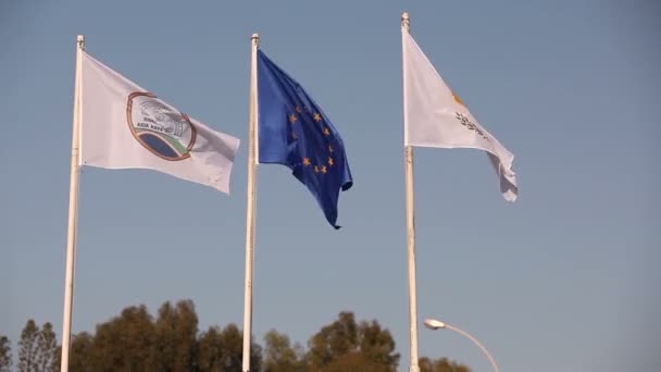 Banderas de la Unión Europea, Grecia, Chipre, la ciudad de Aya Napa, Grecia, Banderas en el asta de la bandera, el viento ondeando la bandera, Banderas en el asta de la bandera, la bandera ondeando viento, contra el fondo del cielo azul — Vídeo de stock
