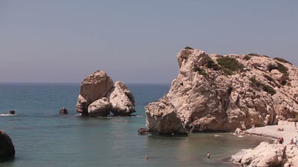 Menschen baden und sonnen sich an einem kleinen Sandstrand, dem Geburtsort des Aphroditen auf der Insel Zypern, Felsen ragen aus dem Meerwasser, schöner Strand im Mittelmeer, felsiger Strand — Stockvideo