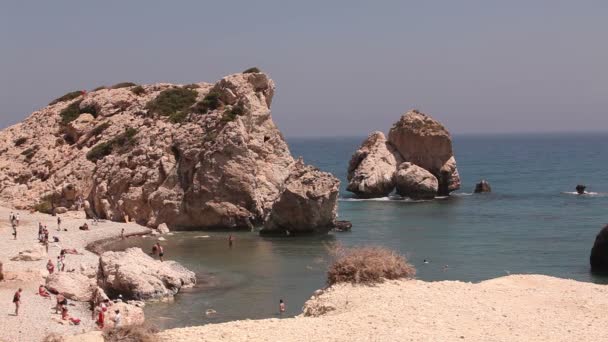 Άνθρωποι να κολυμπά και να κάνετε ηλιοθεραπεία σε μια μικρή αμμώδη παραλία, η γενέτειρα της Αφροδίτης στο νησί της Κύπρου, βράχια ραβδί έξω από το νερό στη θάλασσα, όμορφη παραλία στη Μεσόγειο θάλασσα, βραχώδη παραλία — Αρχείο Βίντεο