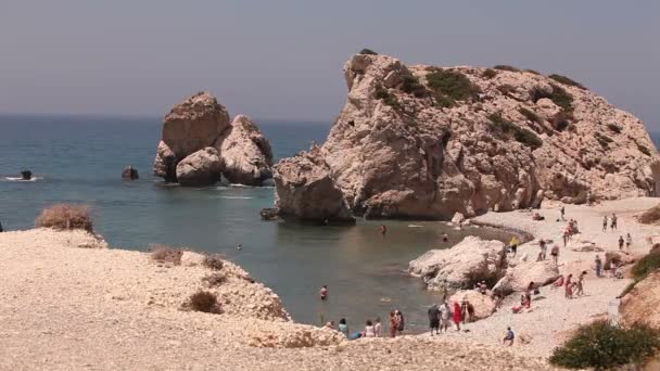 Люди купаются и загорают на небольшом песчаном пляже, родине Афродиты на острове Кипр, скалы торчат из морской воды, Красивый пляж в Средиземном море, скалистый пляж — стоковое видео