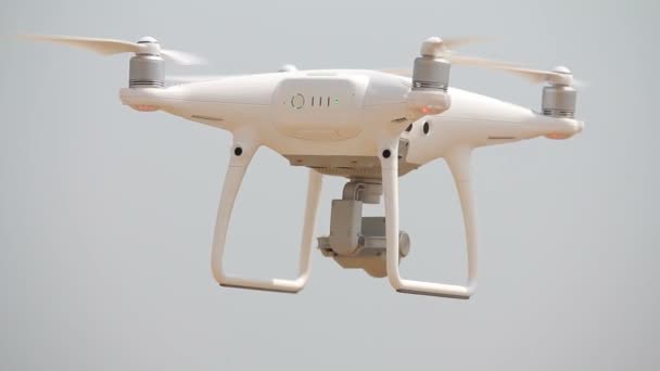 Quadricóptero branco flutua no ar, moscas quadricópteros, hélices girando, quadricóptero pairando sobre o solo — Vídeo de Stock