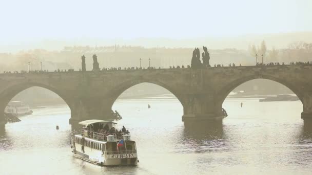 Turistas en el puente Charles, puente Charles. Praga con el telón de fondo de un barco turístico al atardecer — Vídeos de Stock