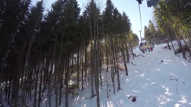 Uno skilift porta la gente sulla montagna, gli sciatori scendono dalle montagne innevate, la gente sta sciando, alti abeti rossi sulla collina, giornata di sole, dalla prima persona — Video Stock