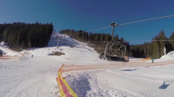 En skidlift bär människor upp på berget. Skidåkare härstammar från de snötäckta bergen. Människor skidåkning, höga granar på bergssluttningen, solig dag — Stockvideo