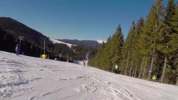 滑雪者来自雪山, 滑雪缆车载人上山, 滑雪者从雪山下山, 人们在山上滑雪, 高高的云杉, 阳光明媚的日子 — 图库视频影像
