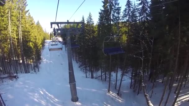 Um teleférico leva pessoas para a montanha. Os esquiadores descem das montanhas nevadas. As pessoas estão esquiando, abetos altos na encosta, dia ensolarado — Vídeo de Stock