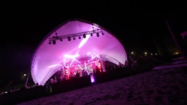 Stage and a disco on the beach. Night Beach Disco with illumination. concert. Celebration. holiday. feast. Dancing people with fun gladness on the discotheque entertainment. sandy beach — Stock Video