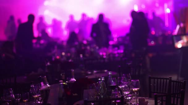 Uma festa de juventude em um restaurante ou uma boate, mesas de banquete com álcool e comida no fundo de silhuetas de pessoas dançando, luz de palco e preenchimento roxo — Vídeo de Stock