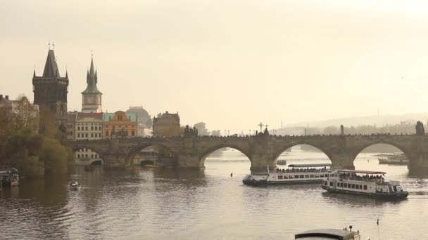 Turistas en el puente de Carlos, Praga con el telón de fondo de un barco turístico al atardecer, plan general — Vídeos de Stock