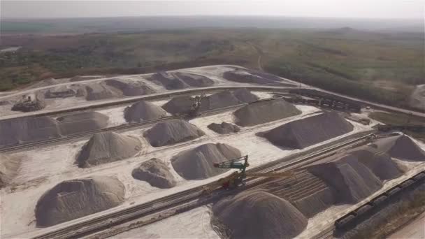 Vista aérea, maquinaria que trabaja en la cantera de arcilla, cargadoras pesadas, camiones grandes, topadoras, excavadoras, cantera de arena, minería, el tren toma materias primas de la cantera, almacén de arcilla grande — Vídeo de stock