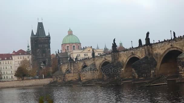 Karlův most na pozadí staré věže a zelené kopule katedrály v Praze, boční pohled, turisté projít Karlův most, Praha, 19. října 2017 — Stock video