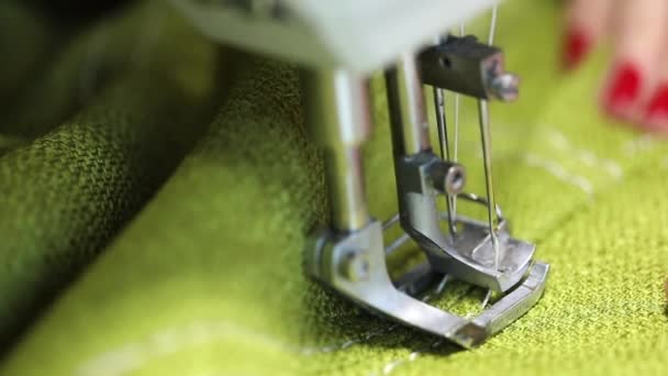 femme travaillant à une machine à coudre, machine à coudre à deux aiguilles, manucure rouge sur les mains féminines, vidéo au ralenti, gros plan, faible profondeur de champ 