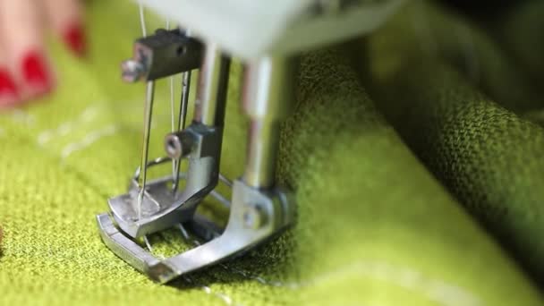 femme travaillant à une machine à coudre, machine à coudre à deux aiguilles, manucure rouge sur les mains féminines, vidéo au ralenti, gros plan, faible profondeur de champ 