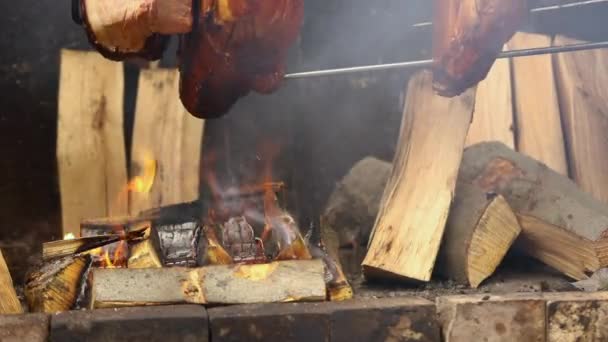 Grandes trozos de deliciosos jamones de cerdo cocinados en una fogata. La comida callejera. Comida al aire libre. Acampar y cocinar en una saliva sobre el fuego, el hombre cocina grandes trozos de carne en una saliva en el fuego, primer plano — Vídeos de Stock